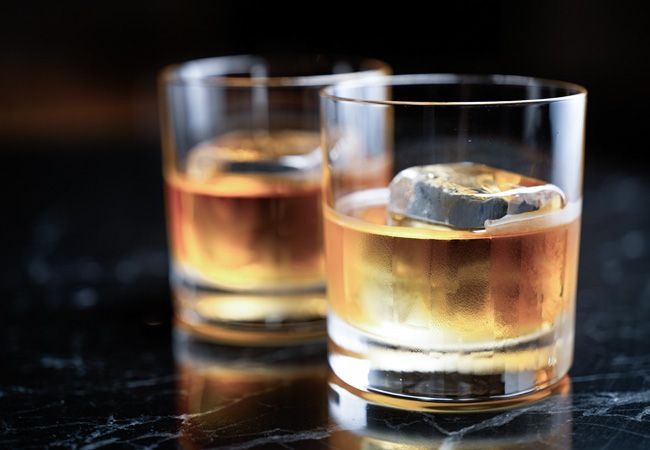 Два стакана с янтарным виски и крупными кубиками льда стоят на тёмной мраморной поверхности